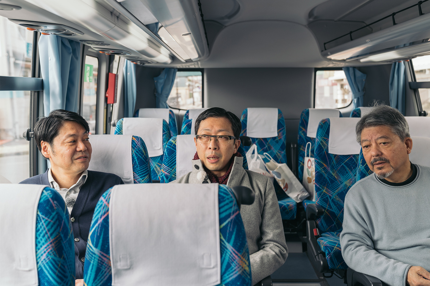 貸切バスで「うのすまい・トモス」に向かう、野村万蔵さん（左）、古今亭菊之丞さん（中）、一般社団法人チームスルマイル代表理事・矢内廣（右）。